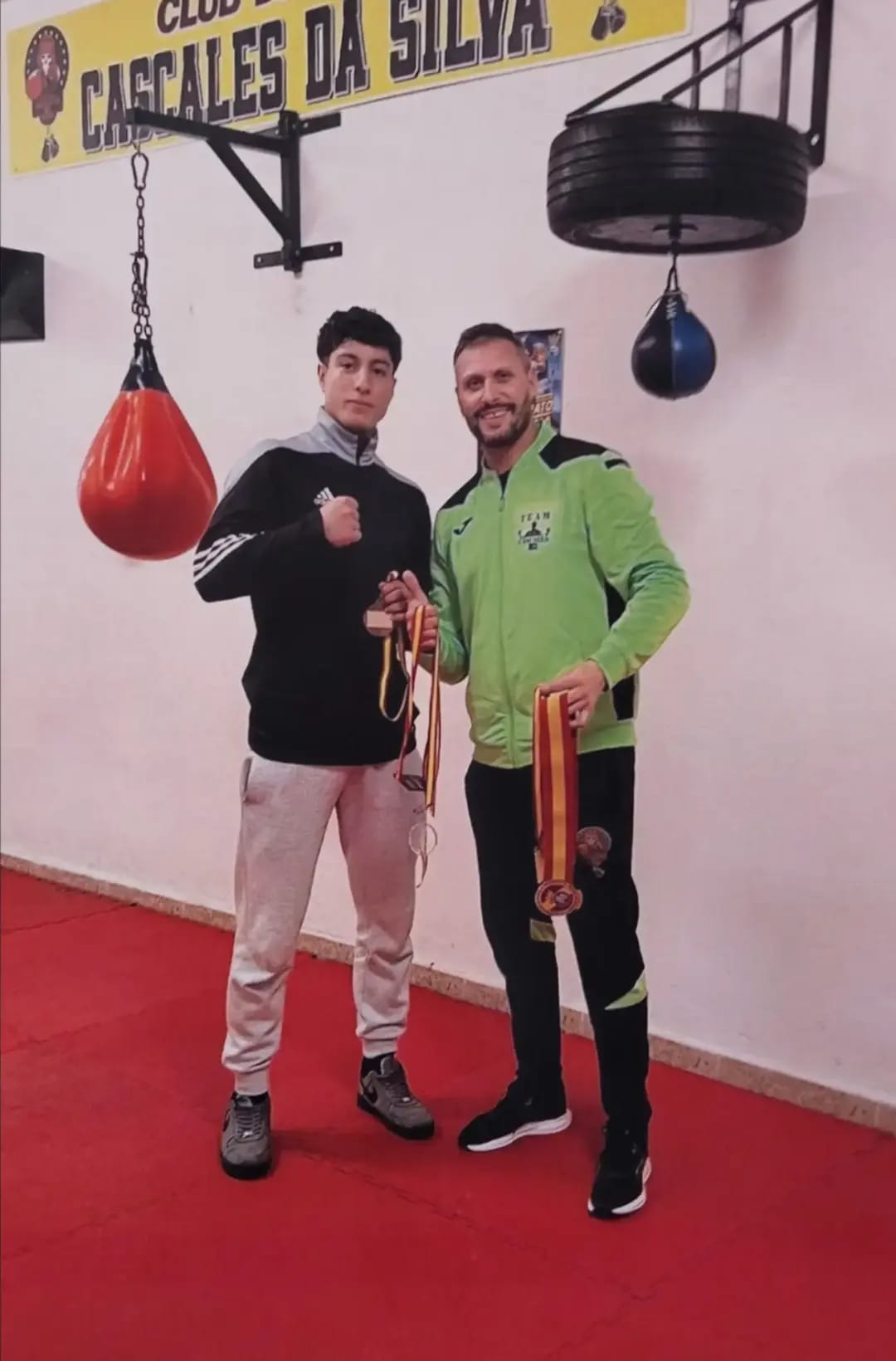 Dos miembros de la escuela con medallas junto al material de entrenamiento